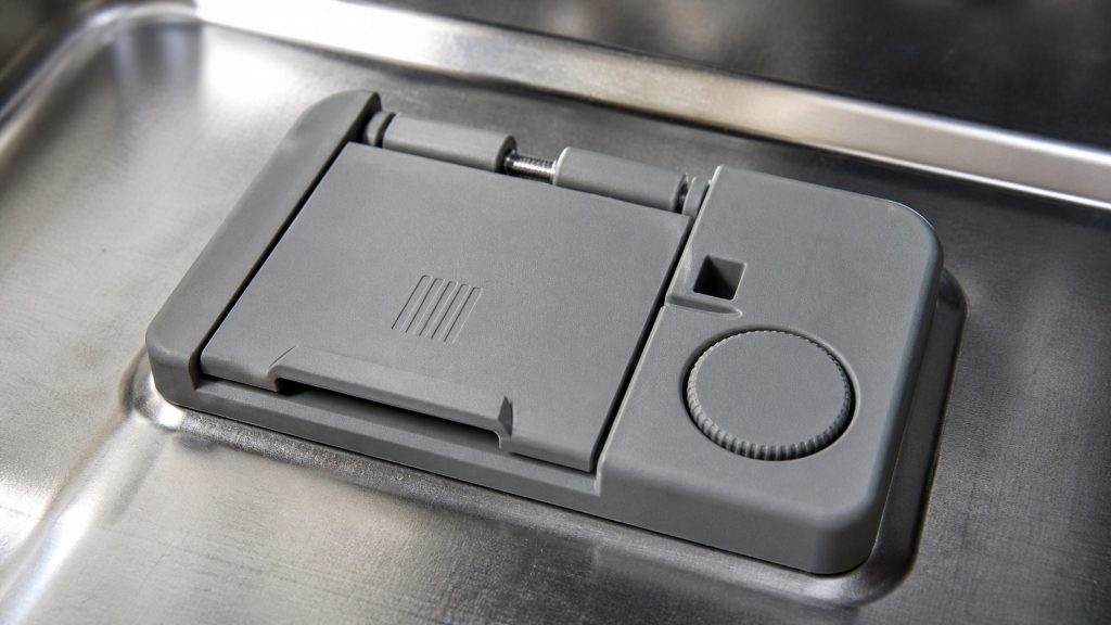 The combined detergent and rinse-aid dispenser molded into a dishwasher's inner door, with its sprung flap and dosage wheel