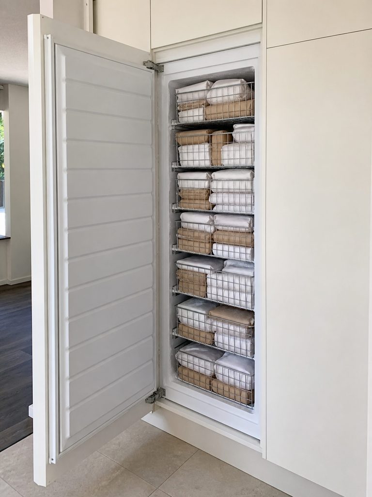 An all-freezer column standing open on wire baskets stacked floor to top, packed with wrapped parcels