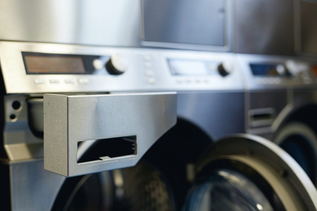 The detergent drawer of a stainless professional washing machine pulled open below its control panel