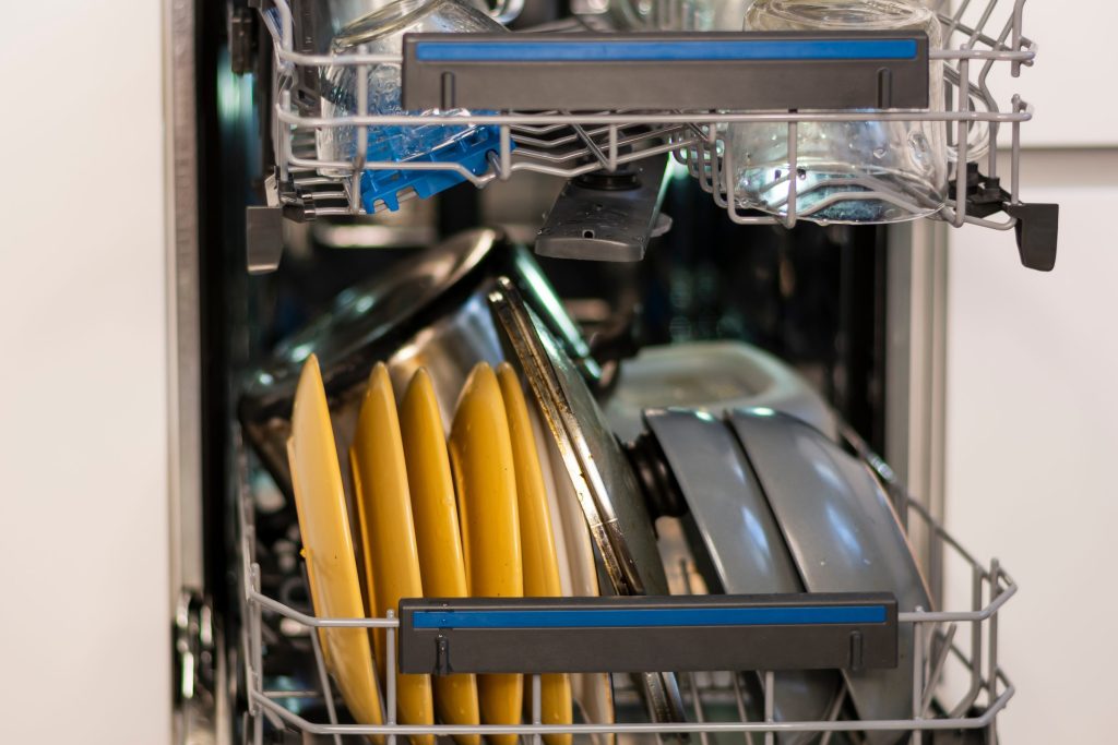 Yellow and dark plates standing on edge in the lower rack of an open dishwasher