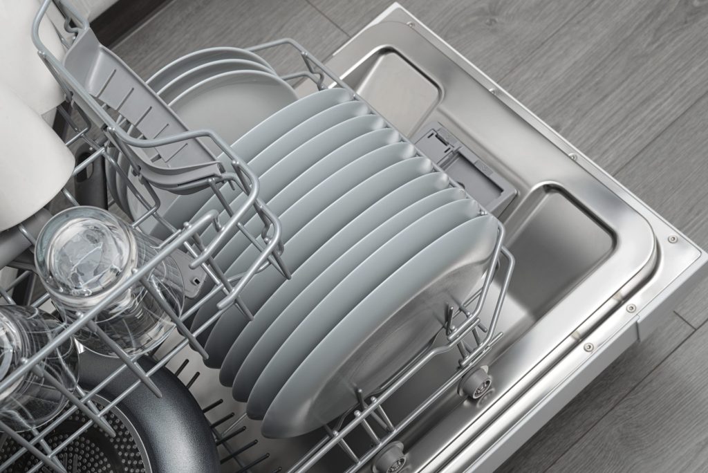 Looking down into an open dishwasher, grey plates on end in the lower rack and glasses at the left