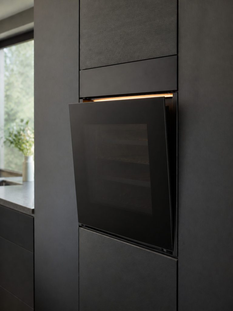 A handleless built-in oven flush in a dark column, its door open a hand's width on the push-to-open catch