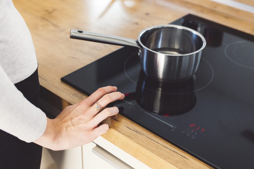 A hand at the touch controls of an induction cooktop in a wood counter, a pan on the ring