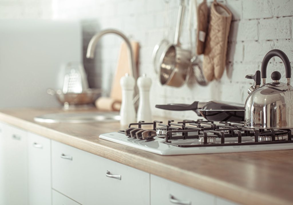 A kettle on a gas hob above a built-in oven in a cream kitchen