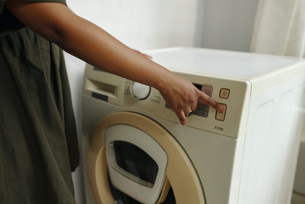 A finger on the start button of a washing machine, the control panel and door below