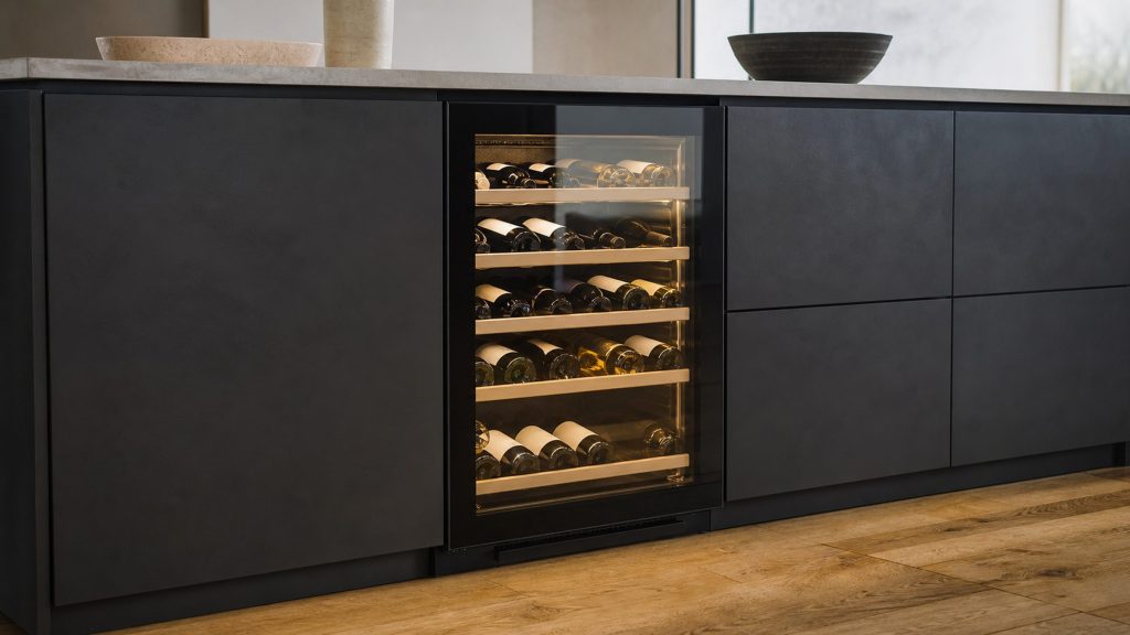 An under-counter wine cabinet lit behind its glass door in a run of dark handleless cabinets