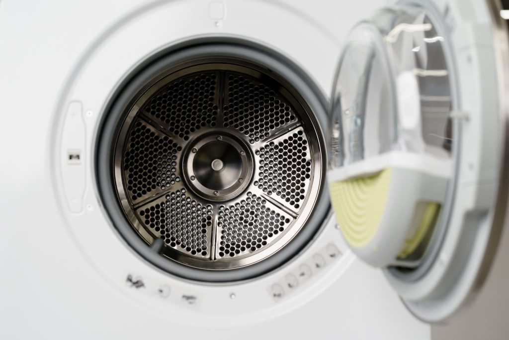 A tumble dryer standing open, the perforated stainless drum and its vanes lit from the door