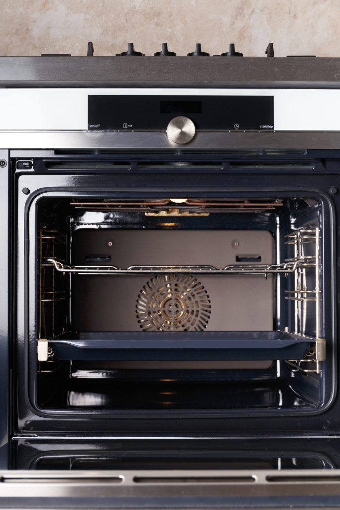 A built-in oven standing open on an enamelled cavity, the fan cover at the back, a tray on the lowest runner