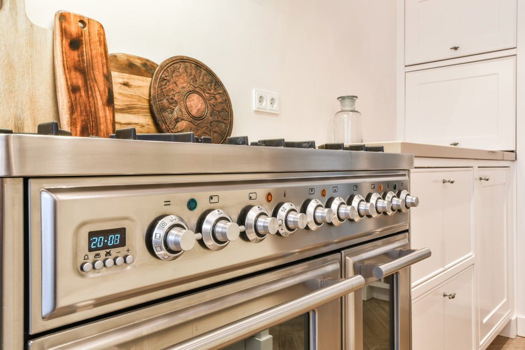 The control fascia of a stainless range: a row of knurled knobs, program symbols and a blue clock