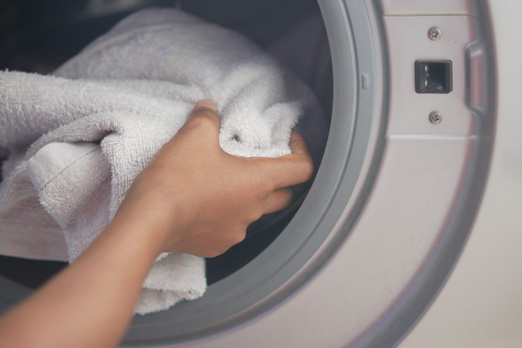 A hand pushing a white towel past the door seal into a washing machine drum