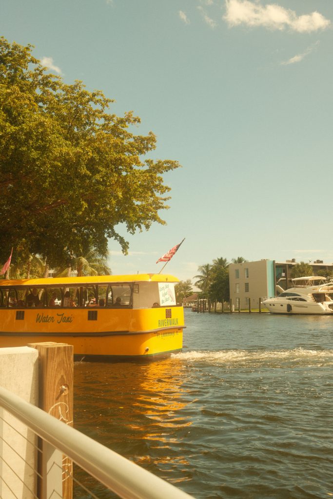 A yellow water taxi on the waterway, with a yacht moored behind it