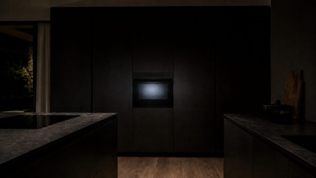One appliance display glowing pale in an otherwise dark kitchen of black cabinetry and stone