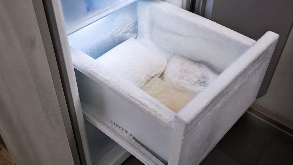 A freezer drawer pulled open on walls thick with frost, the packets inside welded into the ice