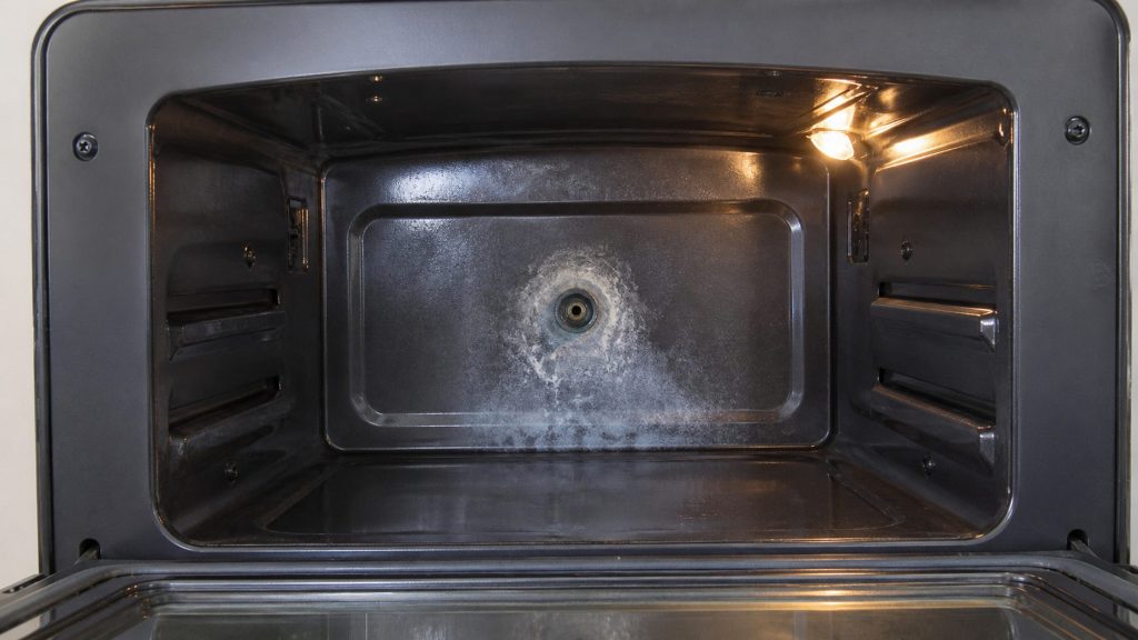 The stainless cavity of a steam oven with a white ring of scale spreading around the steam inlet in its back wall
